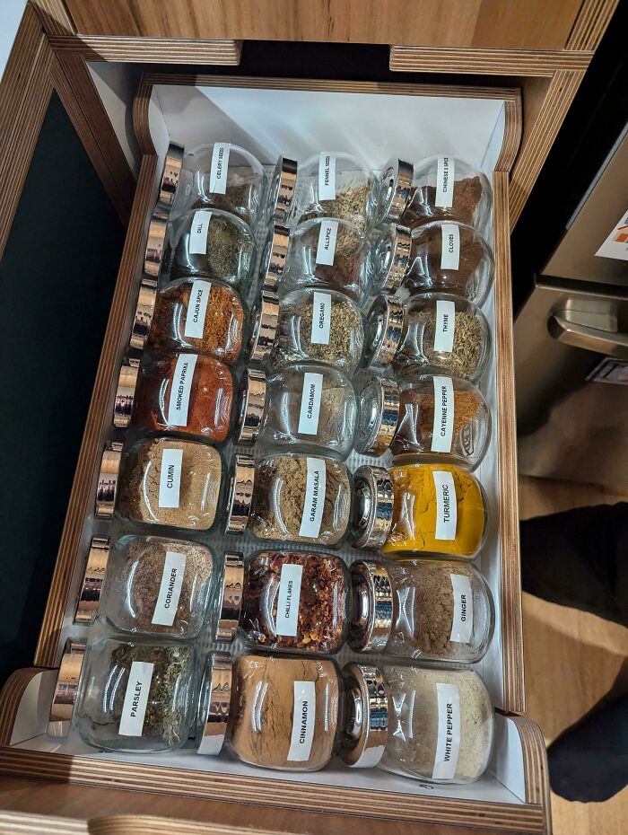 Neat organization of labeled spice jars in a wooden drawer, showcasing next-level arrangement.