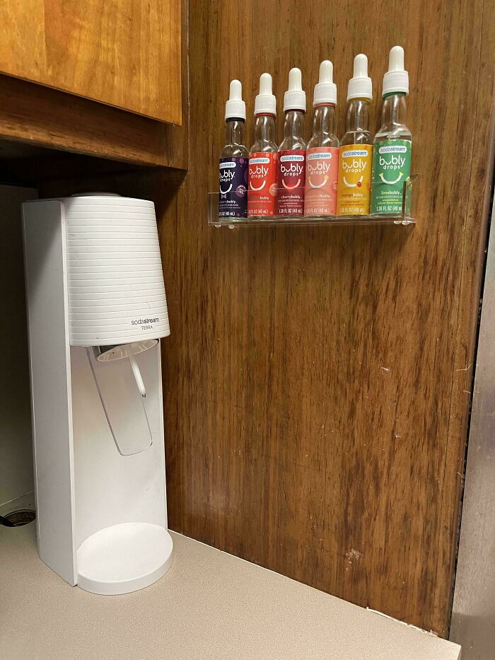 SodaStream machine with neatly organized flavor bottles on a wall rack, showcasing next-level organization.