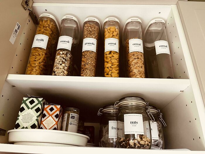Neat pantry organization with labeled jars of pasta, granola, cereal, and nuts on shelves.
