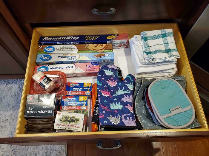Neat results of next-level organization in a kitchen drawer with neatly arranged foil, skewers, and oven mitts.