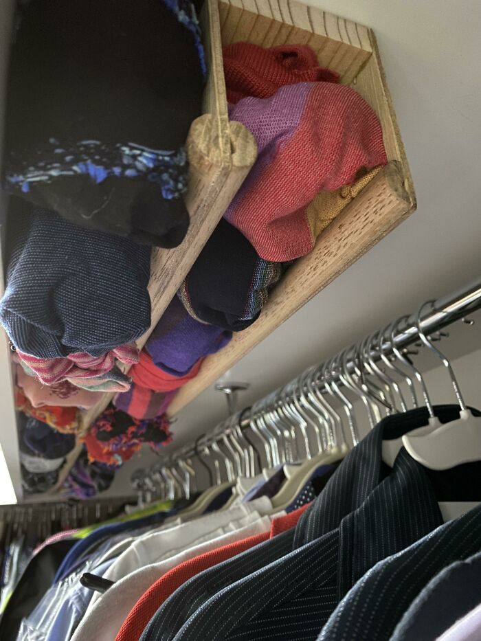 Neat closet organization with rolled-up clothes on shelf and shirts on hangers.