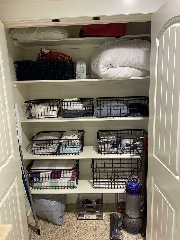 Closet with neatly organized shelves using wire baskets, showcasing next-level organization with linens and cleaning supplies.