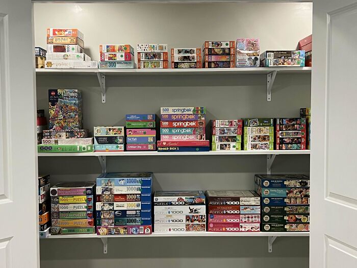 Neat organization of puzzle boxes on three white shelves in a closet.