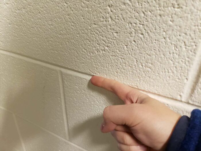 A finger pointing at textured wall blocks, reminiscent of old-school memories.