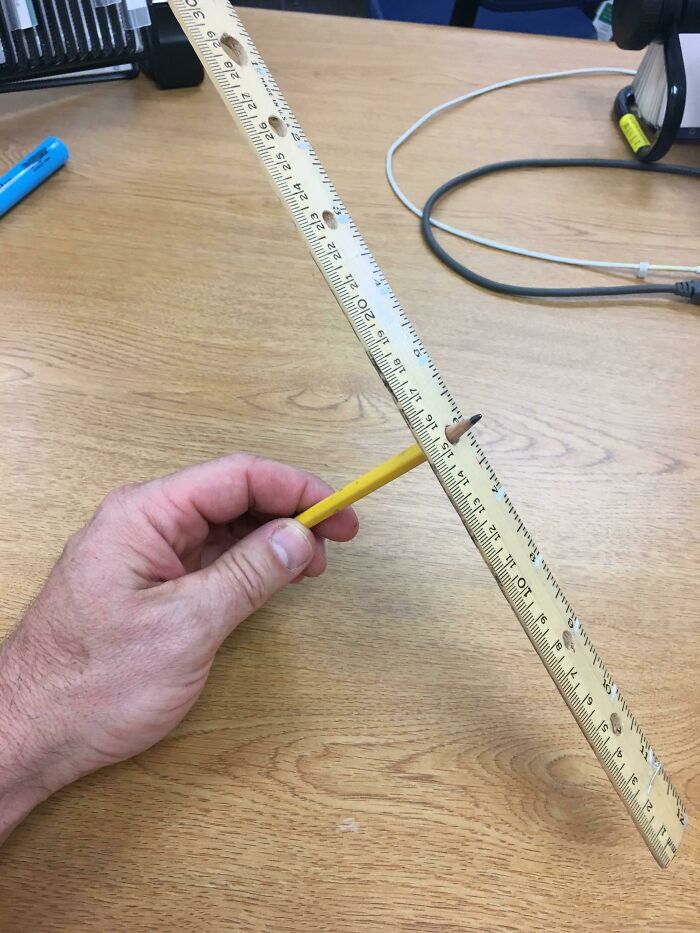 Hand holding a pencil supporting a ruler, showcasing old-school items and memories on a wooden desk.