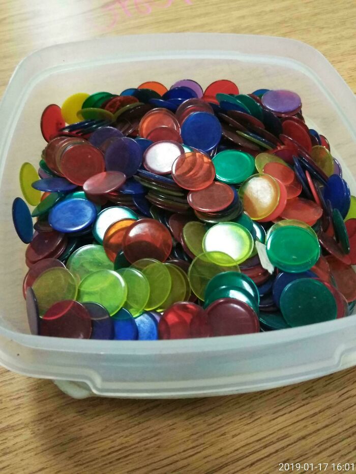 Container filled with colorful plastic tokens on a wooden table, evoking old-school memories.