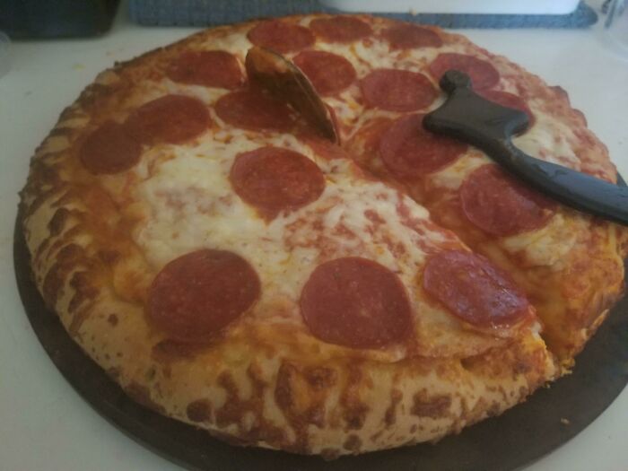 Low-quality pizza with unevenly distributed pepperoni slices and a cutter on top.