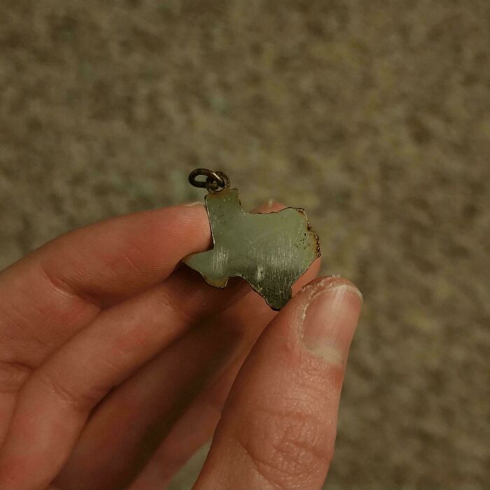 A Texas-shaped pendant held by fingers, showcasing a smart and unusual crow gift.