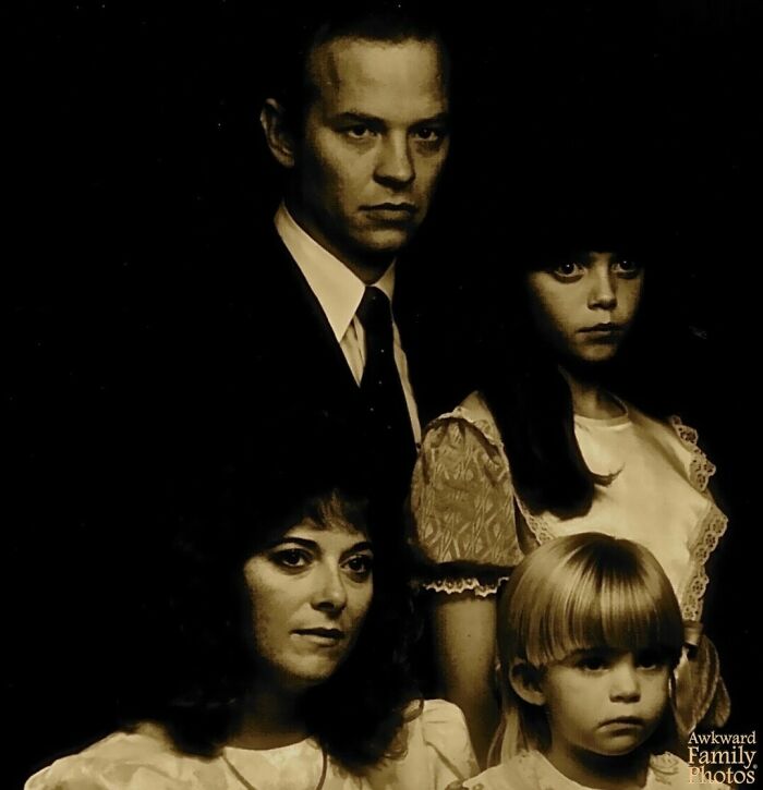 Vintage awkward family photo with serious expressions, capturing an uneasy yet sweet family moment in dim lighting.