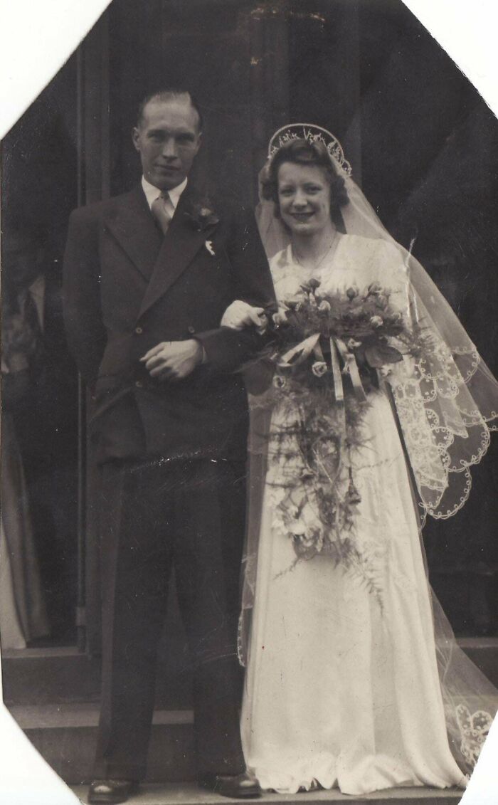 Vintage wedding photo of a bride in a lace veil holding a bouquet, arm-in-arm with groom in a suit.