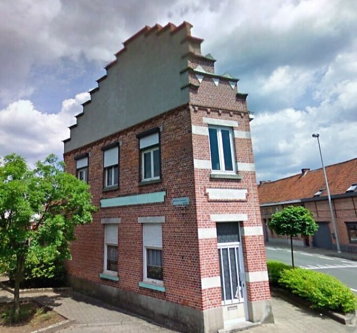 Unusually narrow red brick house with ornate upper design, illustrating hilariously bad architecture in urban setting.