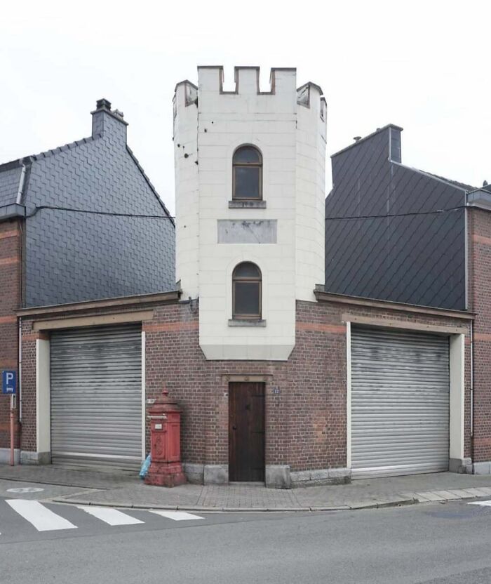 Unusual house with a castle tower facade next to modern buildings on a street corner.