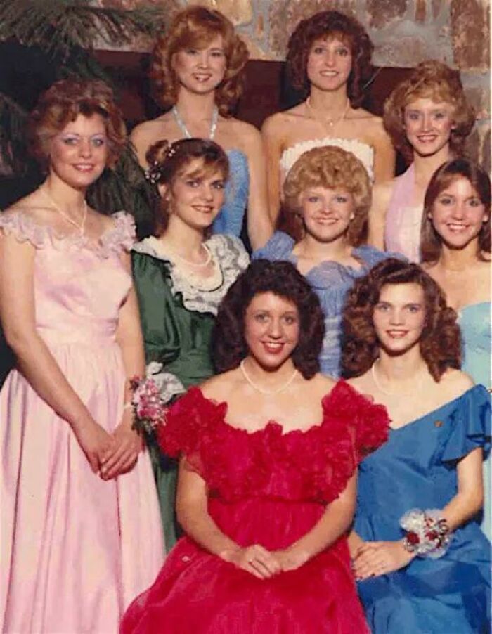 A group of women in 80s fashion trends, wearing colorful dresses with ruffles and puffy sleeves, smiling for a photo.