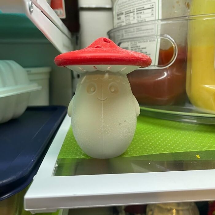 A cute mushroom-shaped fridge deodorizer next to condiments on a refrigerator shelf.