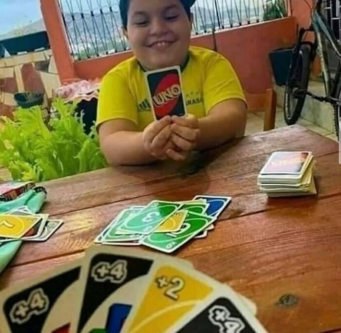 Child smiling and holding an UNO card while playing the weird side of the internet card game outdoors.
