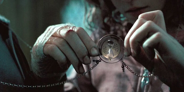 Close-up of hands holding a mysterious locket with an hourglass detail, highlighting questionable movie details in a film scene.