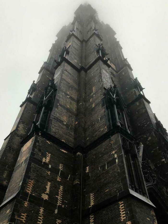 Dark gothic building towering into fog, with an evil aura like a supervillain headquarters in a gloomy atmosphere.