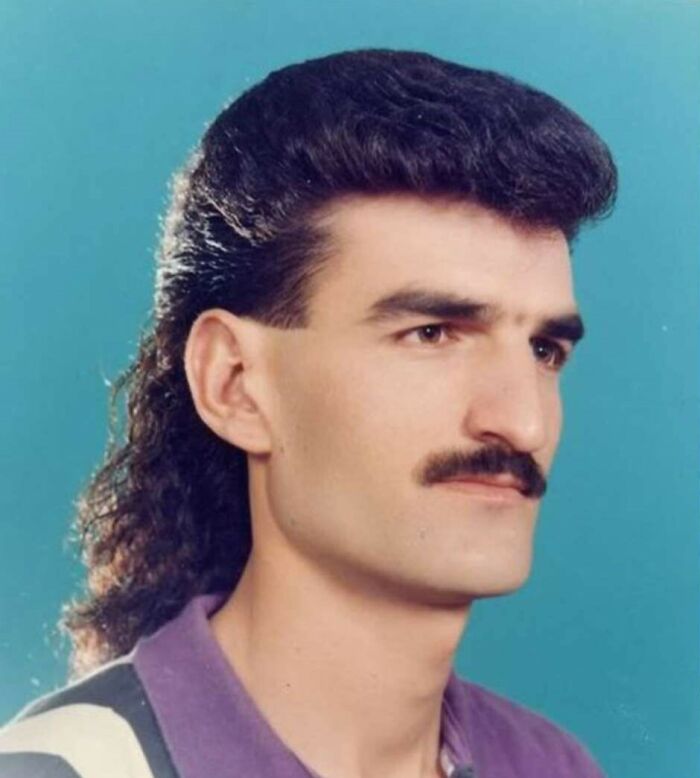 Man with mullet hairstyle and mustache, showcasing 80s fashion trends.