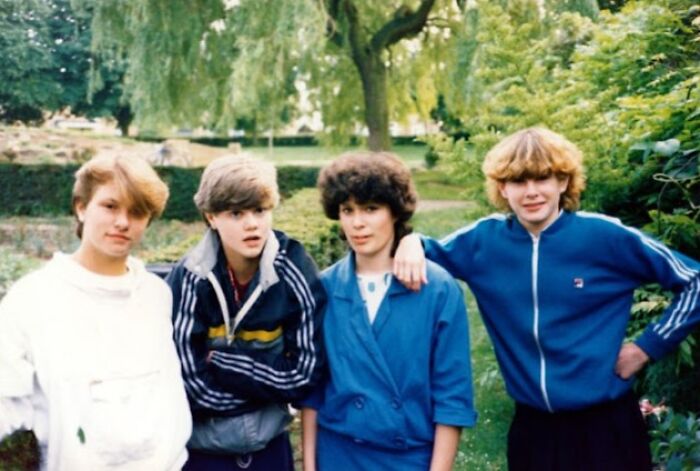 Teenagers in a park wearing 80s fashion trends: track jackets, a blue blazer, and casual hairstyles.