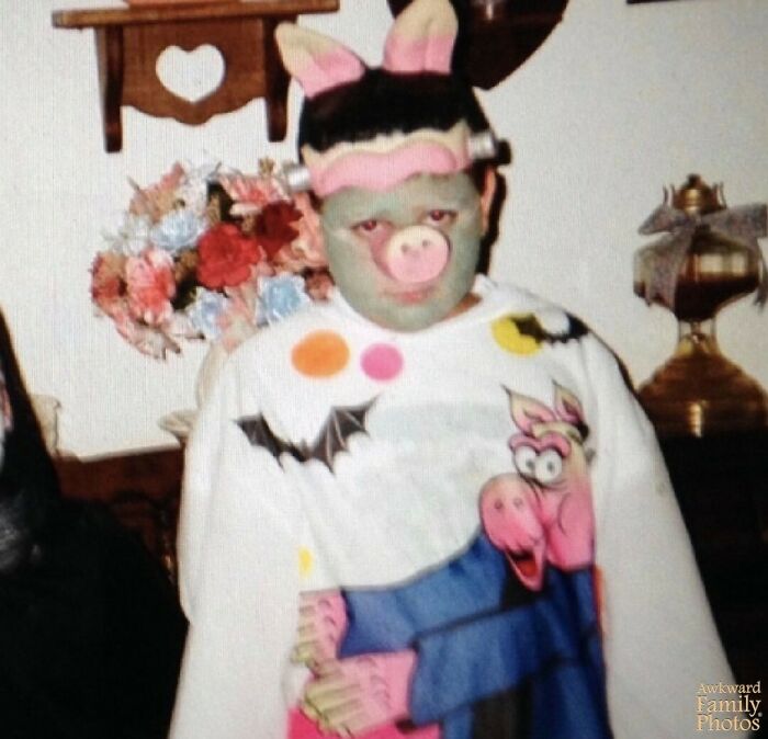 Child in an awkward family photo wearing a pig costume with face paint in a home decorated with flowers and vintage items.
