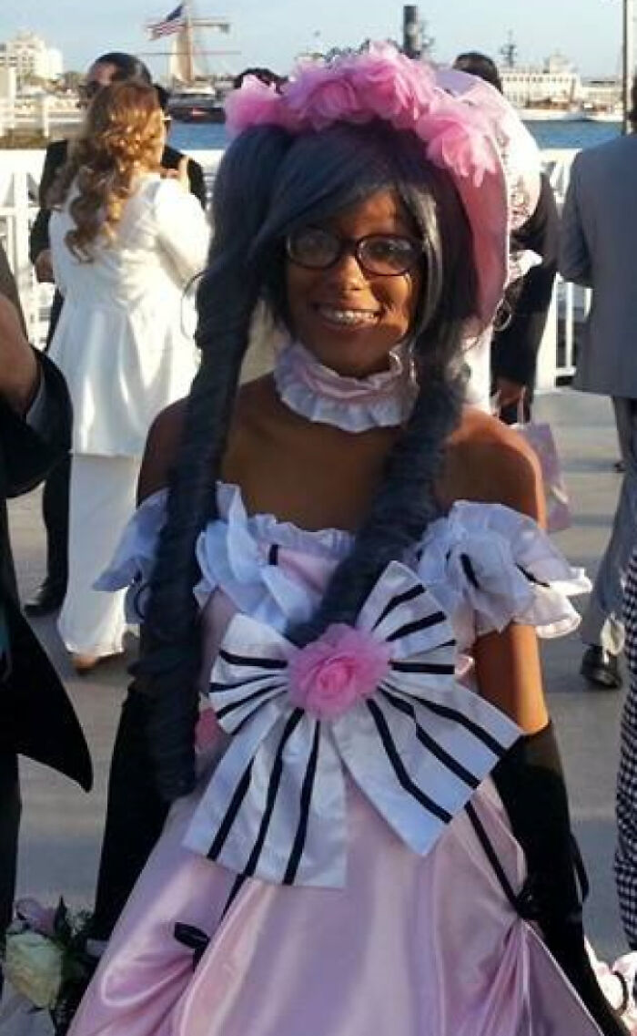 Woman in vintage-style pink dress with large bow, gray wig, and glasses at outdoor event, a cringe-worthy regrettable past look.