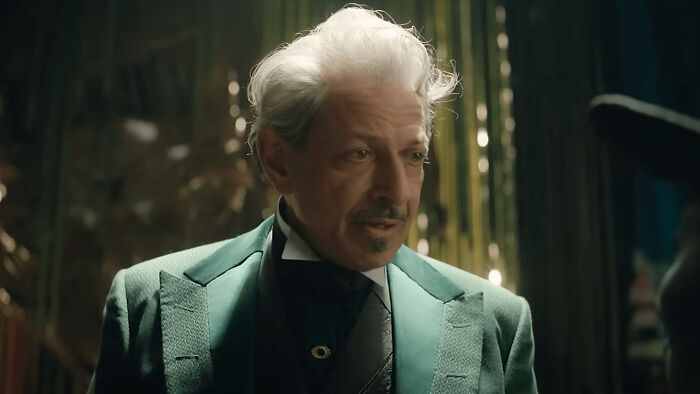 Older man with gray hair and mustache wearing a green suit jacket in a scene highlighting questionable movie details.