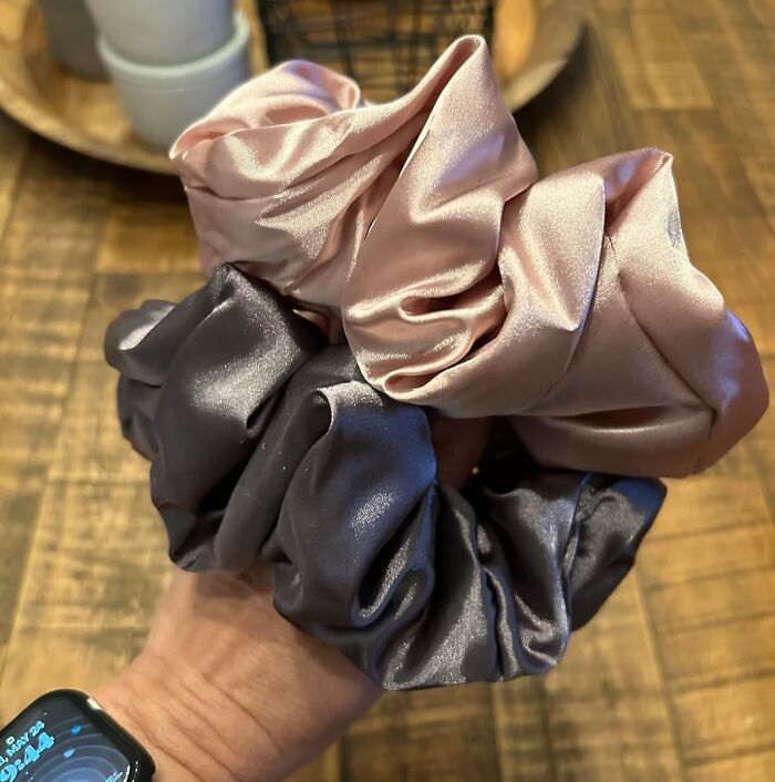 Silk scrunchies in soft pink and gray, ideal for Valentine's Day gifts, held in a hand against a wooden background.