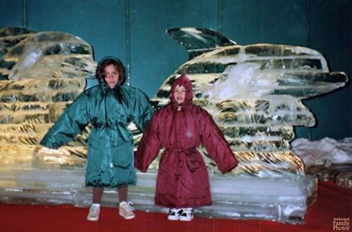 Two children wearing oversized coats posing awkwardly in front of an ice sculpture in an awkward family photo.