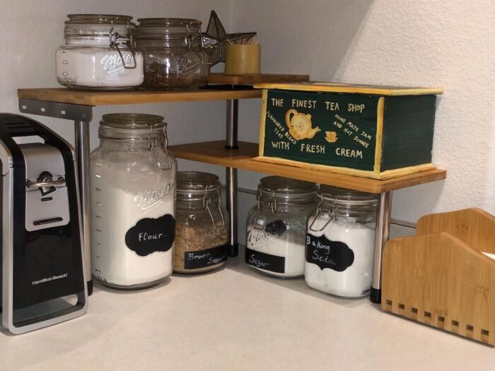 Small kitchen storage with labeled jars and tea box on a corner shelf.