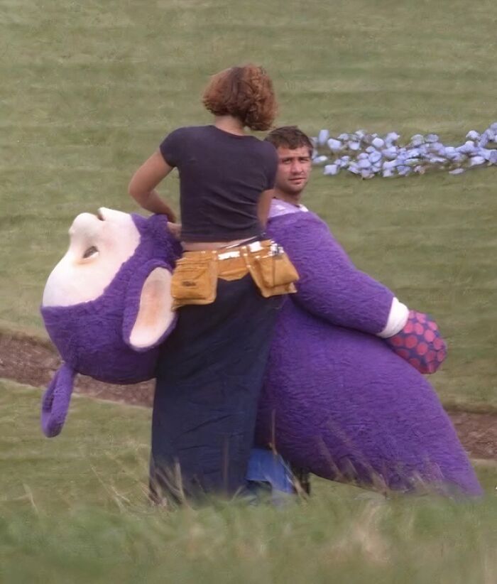 A person adjusts a purple costume for a "History Cool Kids" photo on a grassy set.