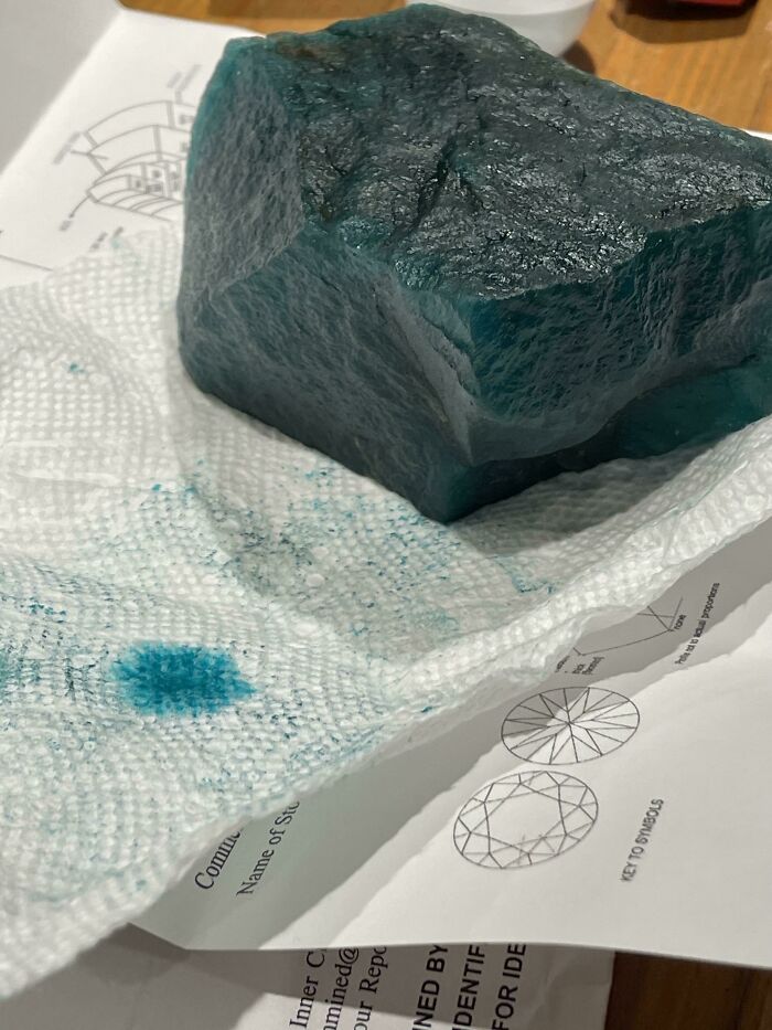 Chunk of raw gemstone from an online shopping scam, placed on a paper towel with blue marks.