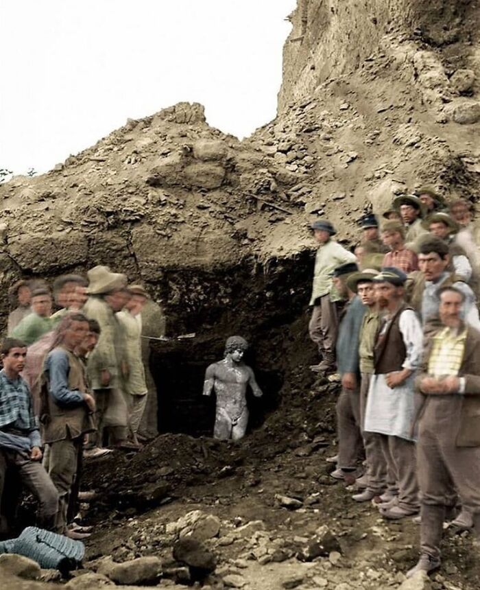 Group of people observing an excavation site uncovering an ancient statue, showcasing cool history moments.