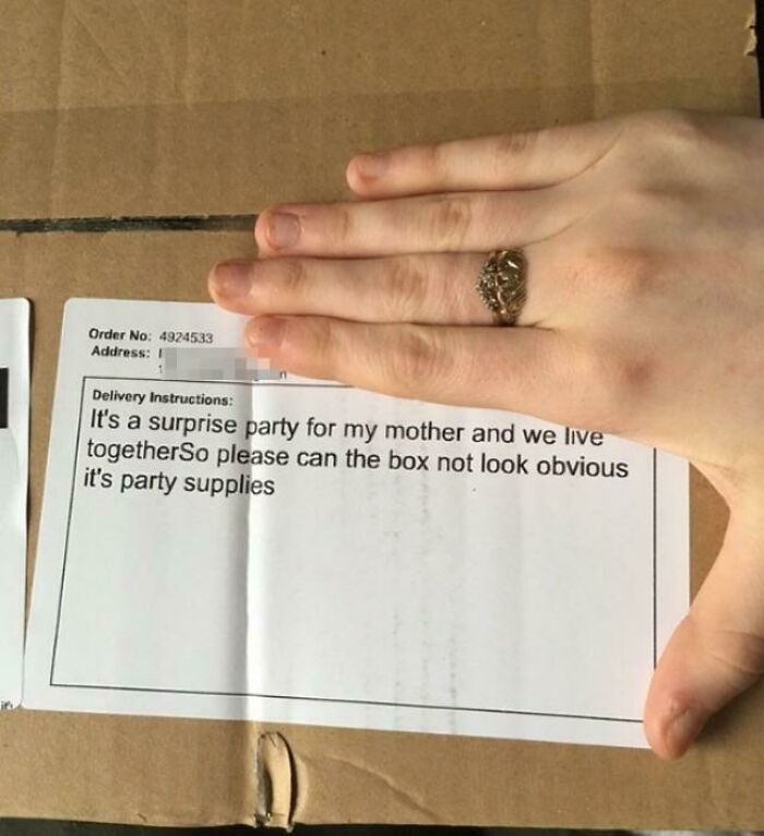 Note with funny delivery misunderstanding on a cardboard box, partially covered by a hand wearing a ring.