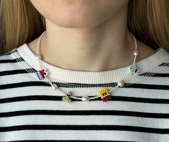 DIY necklace with colorful beaded flowers and pearls on a striped shirt.
