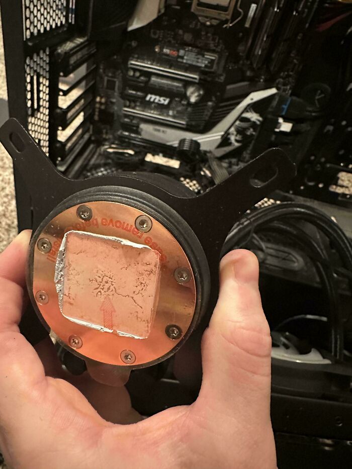 Tech support worker holding a used CPU cooler with thermal paste inside an open desktop computer case.