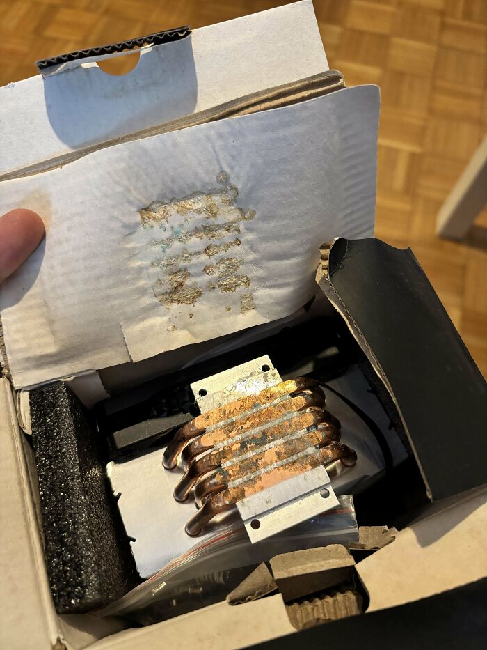 Rusty and corroded computer heat sink with copper pipes inside an opened cardboard box, showing tech support challenges.