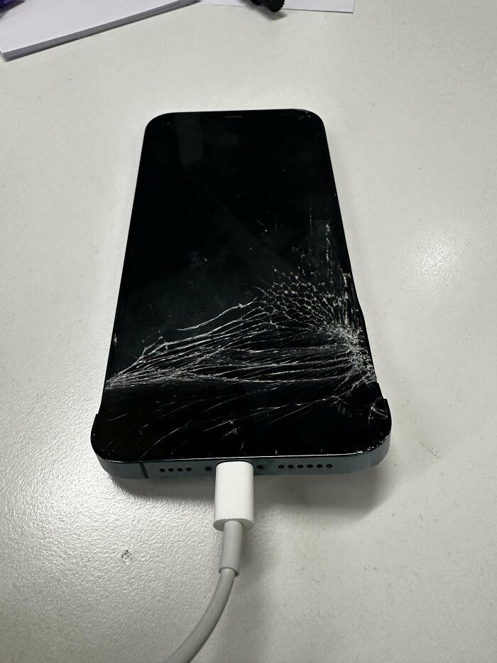 C*****d smartphone screen connected to charger on white desk, highlighting tech support worker challenges and frustrations.