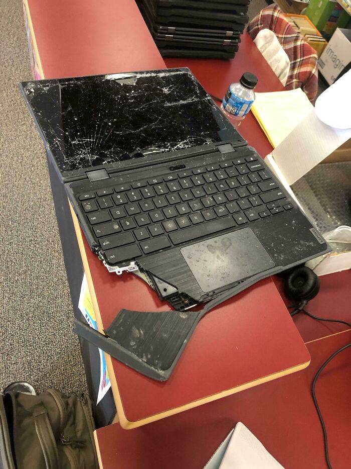 Damaged laptop with c*****d screen and broken keyboard part on a desk, illustrating tech support challenges.
