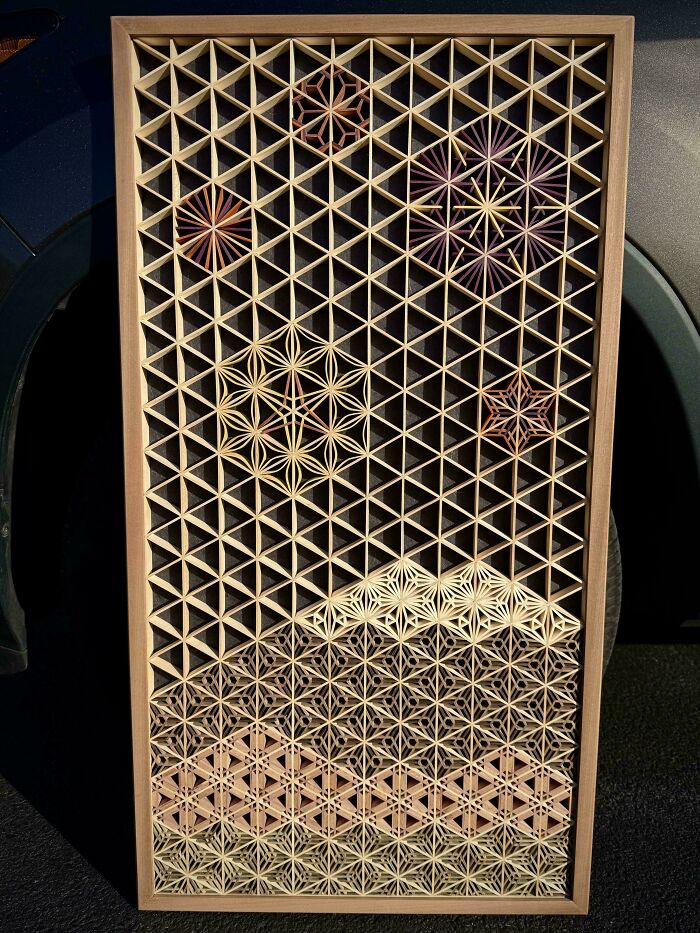 Intricate geometric woodworking project displayed vertically in natural light.