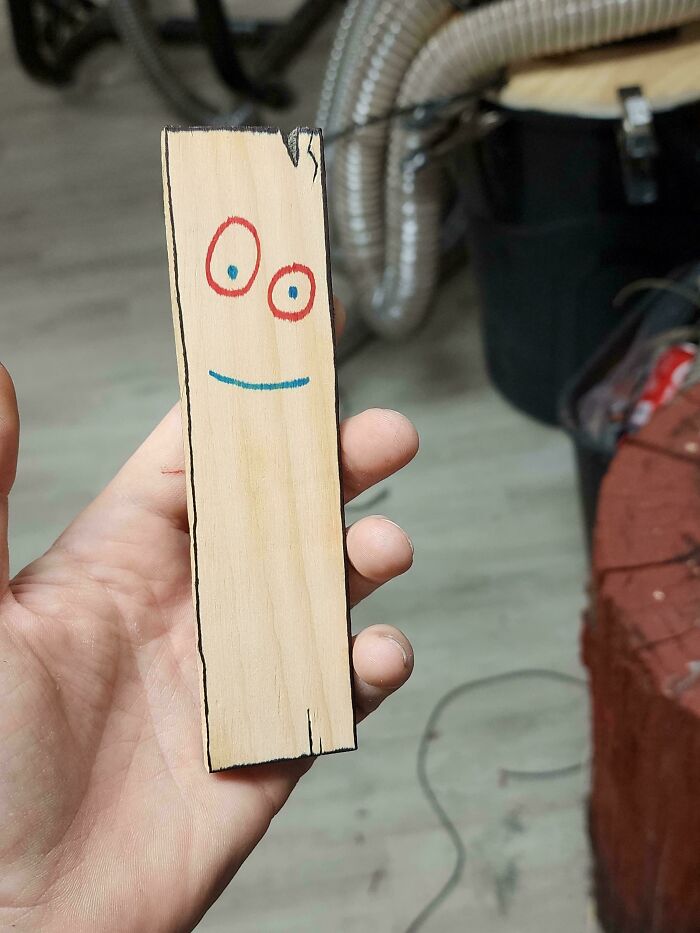 Hand holding a wooden stick with a simple face drawing, highlighting an impressive woodworking project.