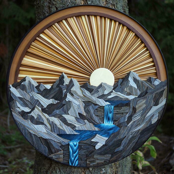 Woodworking project featuring a circular mountain landscape with sunburst and waterfall made from various wood tones.