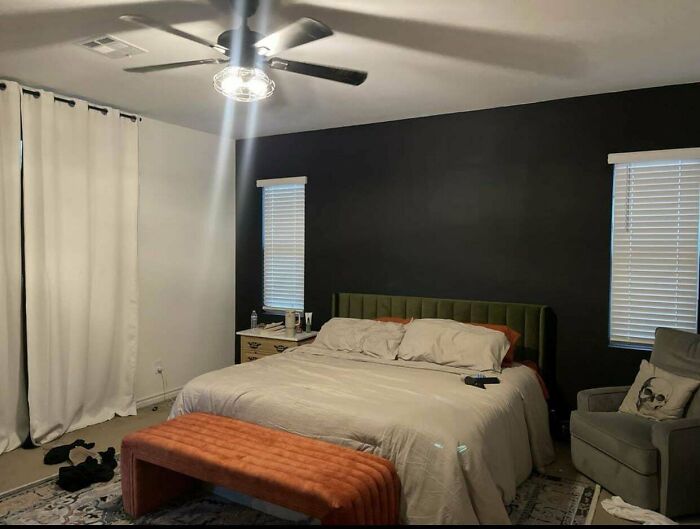 Cozy bedroom with dark accent wall, modern ceiling fan, green upholstered headboard, and warm orange bench at foot of bed.