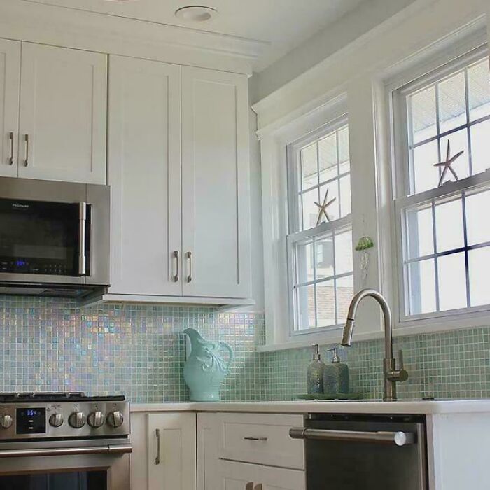 Modern kitchen with beautifully decorated homes featuring white cabinets, mosaic tile backsplash, and stainless steel appliances.