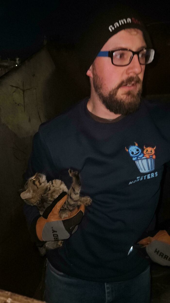 Bearded man holding a tabby cat during a dumpster diving adventure.