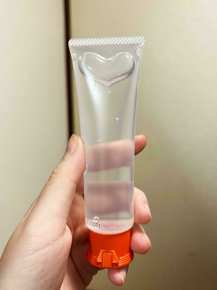 A hand holding an interesting clear tube with a heart-shaped top and red cap.