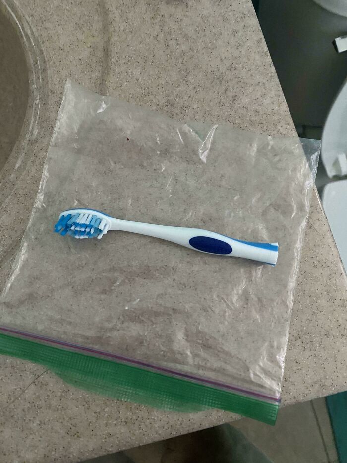 A toothbrush inside a large plastic bag on a bathroom counter, showcasing a mildly interesting contrast in size.