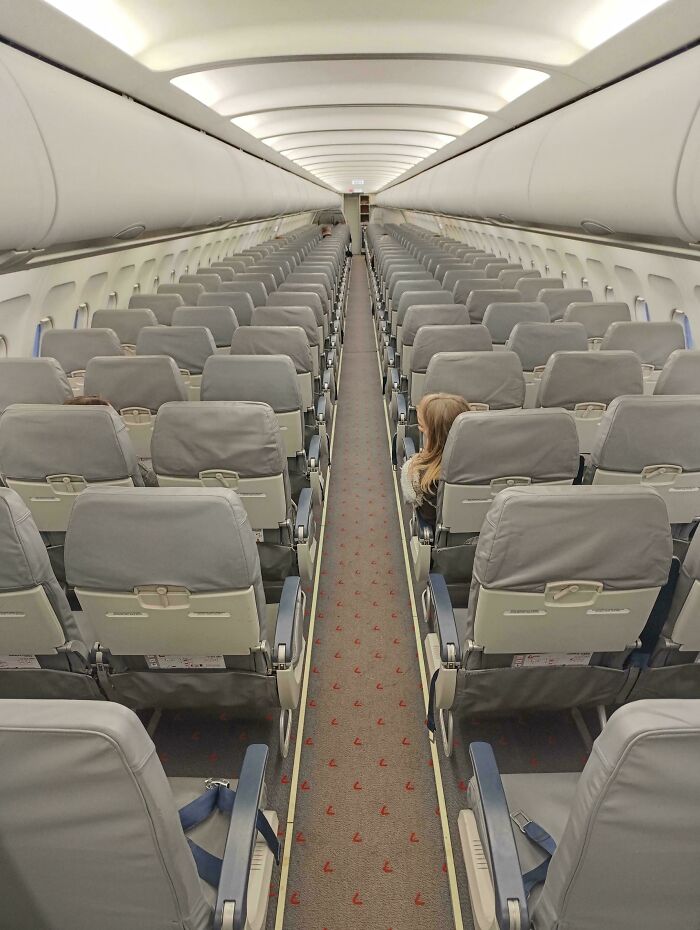 Interior of an empty airplane cabin, showing rows of seats and a lone passenger, offering mildly interesting visuals.