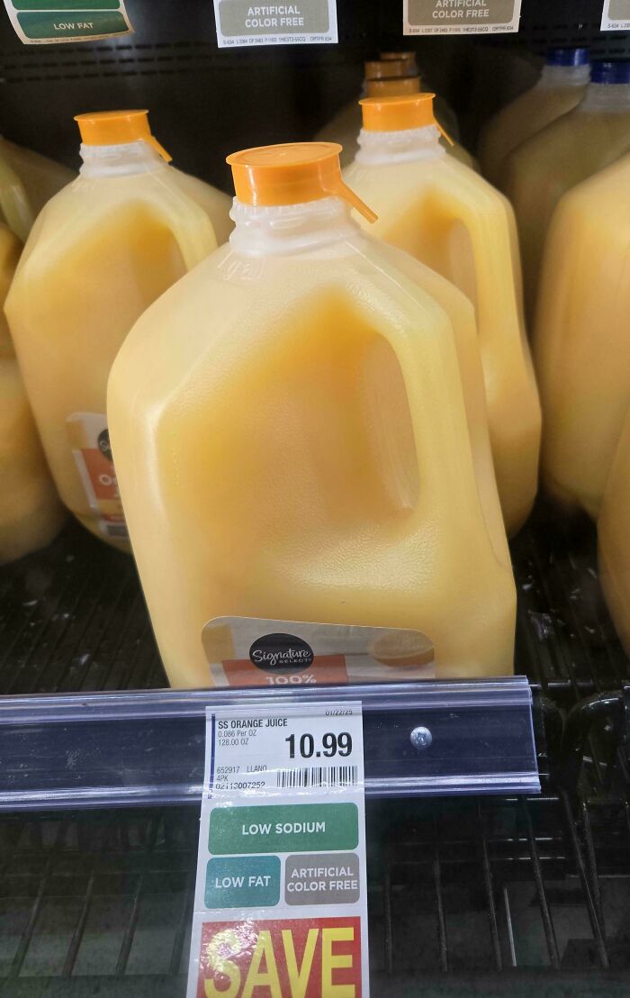 Orange juice jug marked $10.99 on a grocery store shelf labeled low sodium, low fat, and artificial color free for amusement.