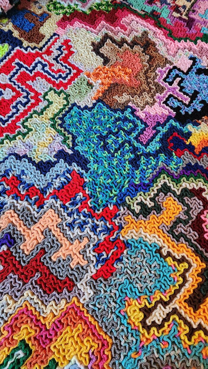 Colorful crochet fabric with intricate textured stitches forming an abstract patchwork of vibrant patterns.