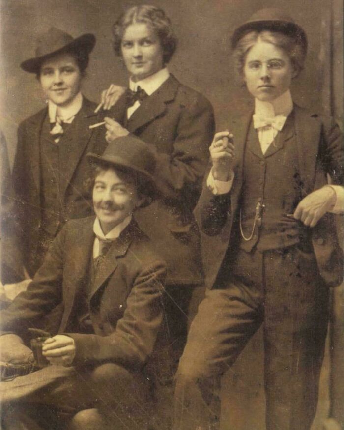 Victorian era women dressed in suits and hats, confidently posing with cigarettes.